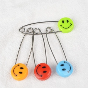 Colorful smiley face baby safety pins in green orange red and blue on white fabric
