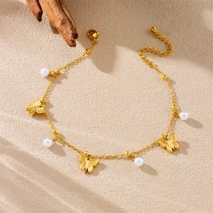 Golden stainless steel anklet with butterfly charms and pearls on sandy background
