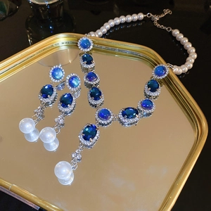 Macro detail of luxury blue gemstone and pearl jewelry set on a golden mirrored tray