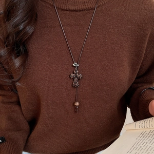 Gros plan d'un collier pendentif croix léopard sur un pull marron vintage