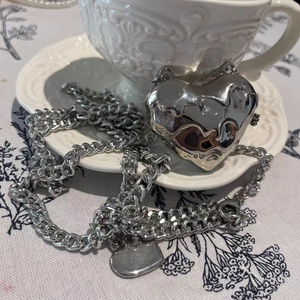 Detail of silver heart-shaped liquid metal pendant by a white decorative porcelain cup