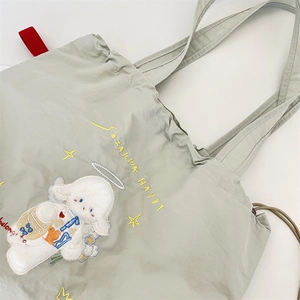 Close-up of embroidered white cartoon lamb and stars on a light green canvas tote bag
