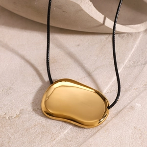 Macro shot of polished gold organic pebble pendant on minimalist black cord necklace