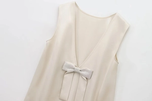 Detail of V-neck sleeveless beige dress with shimmering fabric and rhinestone bow decor