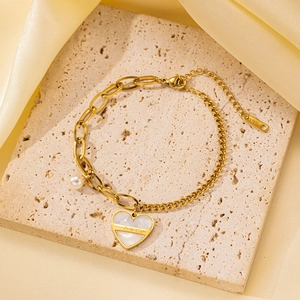 Detalle de la pulsera dorada con colgante de corazón y perla sobre piedra travertino