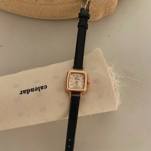 Close-up of a vintage square watch with rose gold case and black leather strap