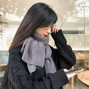 Close-up of a thick grey knit winter scarf paired with a black tweed sweater for women