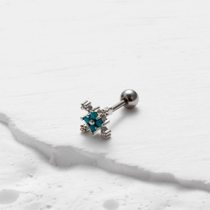 Macro shot of silver cross earring with turquoise stones on a white textured stone surface