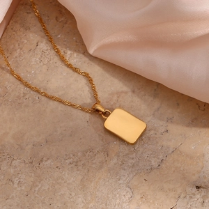 Detail of a gold rectangular pendant on a fine water wave chain over elegant silk fabric