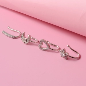 Detailed view of silver ear cuff set with moon, heart, and star designs on pink background
