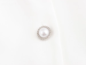 Detail of elegant pearl button with silver metal rim on white fabric vest