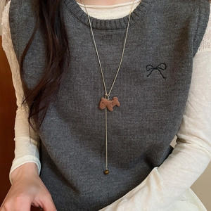 Detail of tiger eye stone horse pendant on long sweater necklace worn over grey knit vest