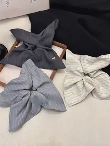 Detailed view of striped fabric bow scrunchies in grey and beige with gold metal charms