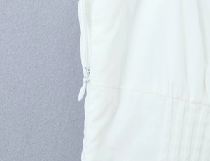 Close-up of white woven dress featuring a concealed zipper and pleated details