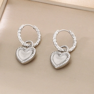 Détail de boucles d'oreilles cœur argentées avec émail blanc et finition martelée