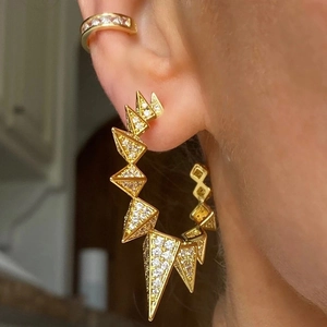 Close-up of gold geometric stud earring and ear cuff with zircons in punk style