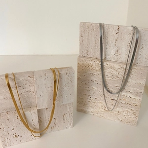 Double-layered gold and silver snake bone chain necklaces on minimalist stone blocks