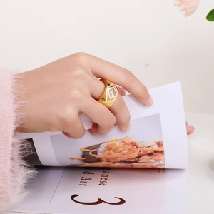 Detail of a wide gold geometric ring with square clear gemstone on a model's hand