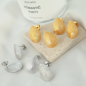 Elegant gold and silver teardrop earrings with textured ripples on marble stone base