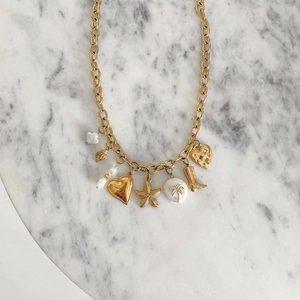 Detailed overhead view of golden charm necklace with pearls and starfish on marble