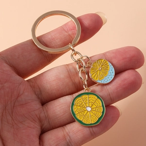 Detail of yellow and green fruit slice keychains with polished metal ring on pink background