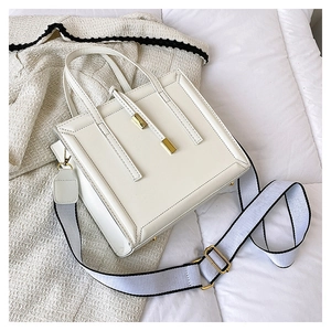 Top view of white square handbag with golden hardware and a wide woven shoulder strap