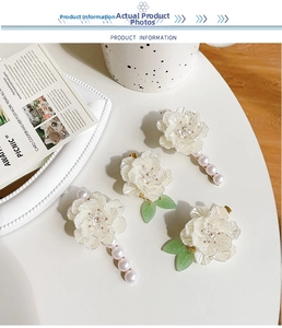 Dettaglio di fermagli per capelli a camelia con perle e foglie verdi su sfondo bianco