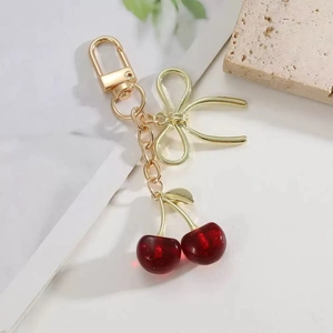 Porte-clés cerise 3D avec boucle en métal doré et nœud élégant sur support pierre