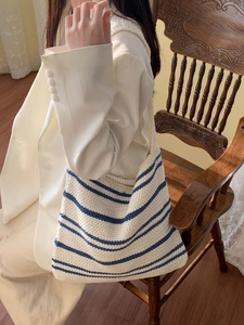 Close-up of cream knit shoulder bag with blue stripes shown on a model in a white blazer