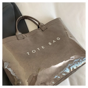 Close-up of minimalist glossy brown leather tote bag with white TOTE BAG slogan on suit