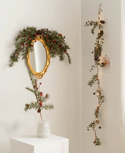 Close-up of Christmas pine needle garland with red berries, pine cones and warm LED lights