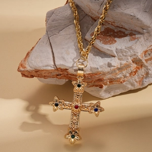 Détail macro du pendentif croix dorée rétro avec strass colorés sur une roche brute