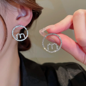 Close-up of silver-tone hoop earrings with pavé crystals and letter M logo design