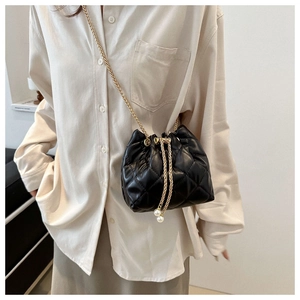 Model wearing a black quilted bucket bag with gold chain and pearl drawstring charms