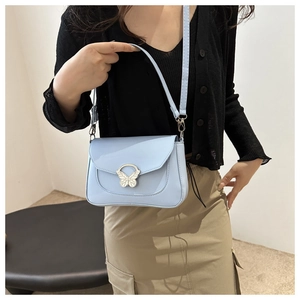 Model wearing a light blue crossbody bag featuring a unique butterfly metal clasp