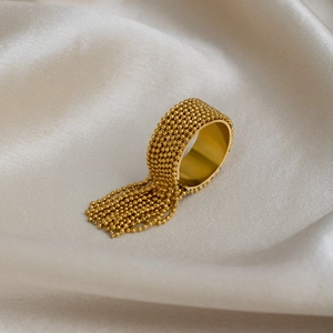 Close-up of gold tassel ring with beaded layers on a luxurious cream silk background