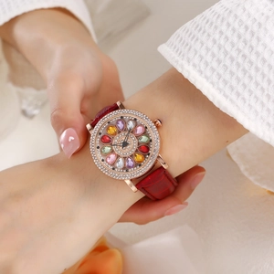 Detail of rose gold watch with colorful gem floral dial and red leather strap on wrist