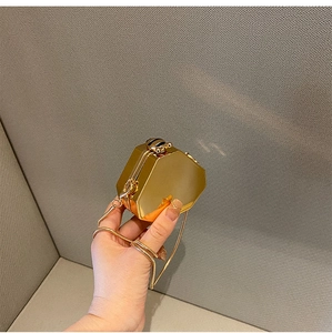 Detail of a mini golden hexagonal metallic evening bag with fine chain held by hand