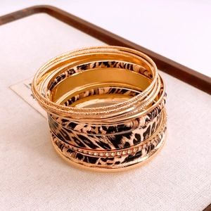 Detail of stacked gold bangles featuring leopard print leather and crystal inlay sets
