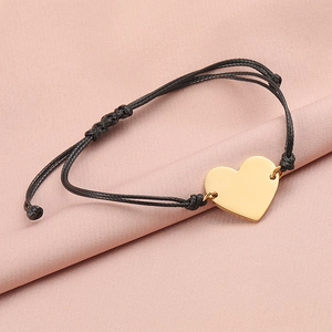 Detail of a golden heart charm on a black braided cord against a pink silk background