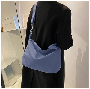 Detail of blue crossbody bag featuring silver metal chain strap on minimalist blazer
