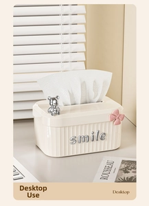 Macro detail of cream tissue box with silver smile text and bear ornament on a desk