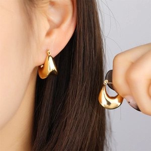 Abstract geometric gold teardrop earrings with a glossy metal finish on a female model