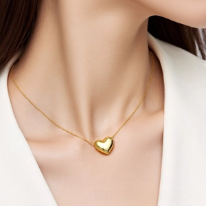 Detailed view of polished gold heart pendant necklace worn on neck with white blazer