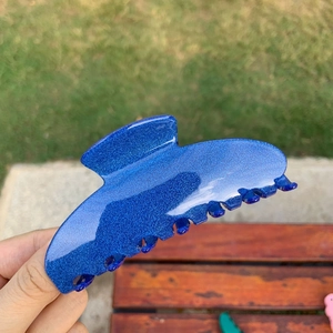 Close-up of blue glitter acetate hair claw clip with seven teeth on outdoor background