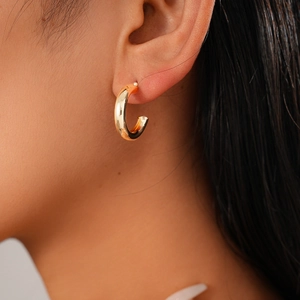Close-up of a minimalist gold C-shaped geometric hoop earring worn by a female model
