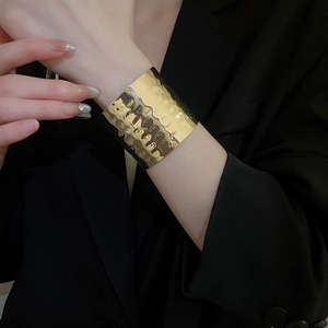 Detailed view of wide gold cuff bracelet with irregular hammered texture on female wrist