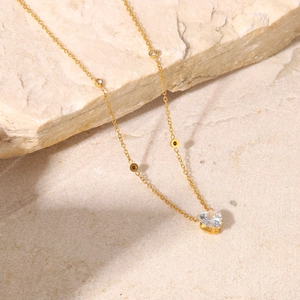 Detailed close-up of 18K gold plated necklace with white heart zircon on beige stone