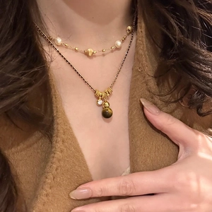 Double-layered gold necklace featuring tiger eye pendant, pearls, and zircon stones on a model