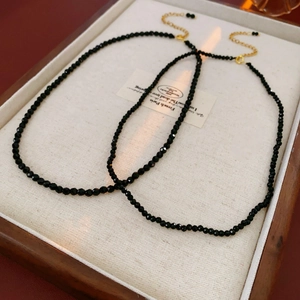 Close-up of two minimalist black beaded necklaces on a wooden tray with gold clasps